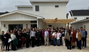 Diverse group of people posing outside a white two-story house under construction with a wooden framework.