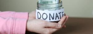 Child's hands holding a glass donation jar with a handwritten DONATE label for charity collection.
