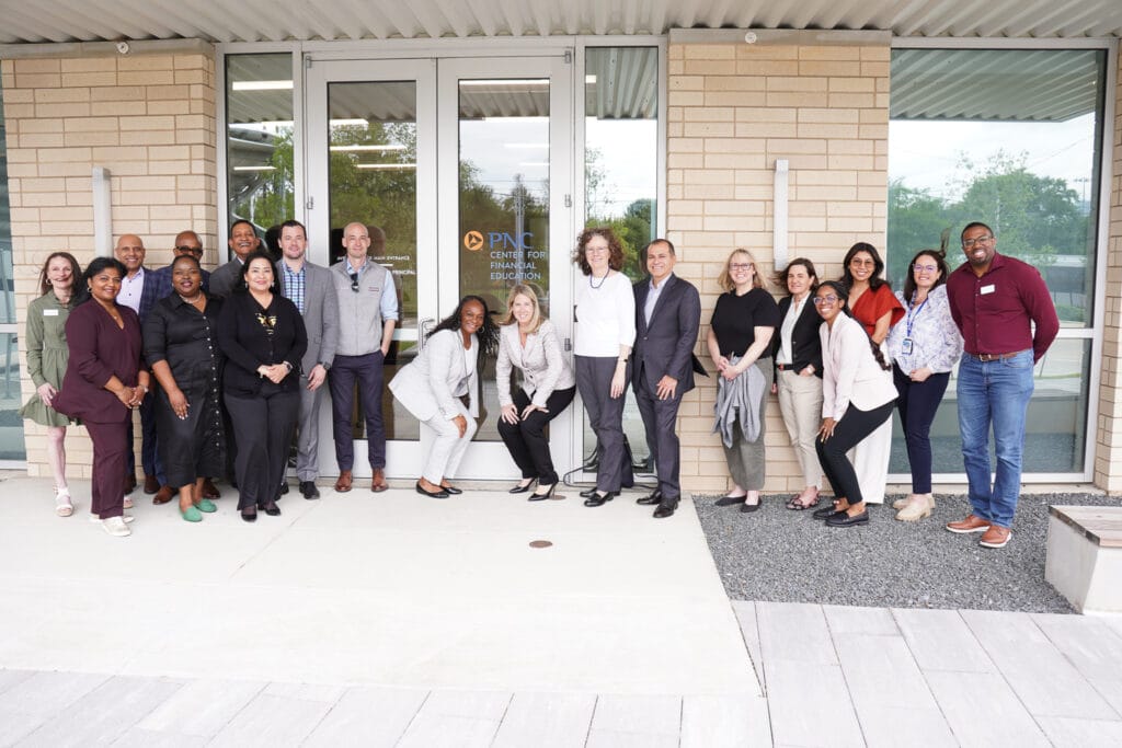 Diverse group of professionals posing outside a brick building in front of glass doors for a team photo.