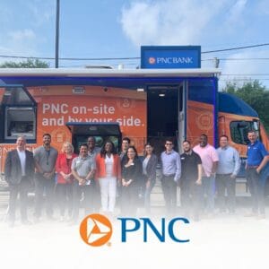 Group of diverse employees posing in front of a PNC on-site mobile banking van with orange branding and a PNC logo in the foreground.